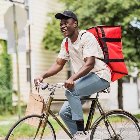 Smiling delivery rider on a bicycle with a large red delivery backpack